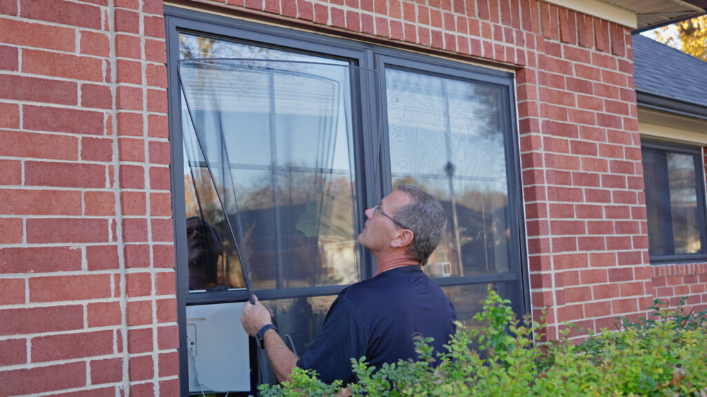 About Us - A professional window installer fitting a new window screen on a brick home, showcasing expert craftsmanship and quality service.